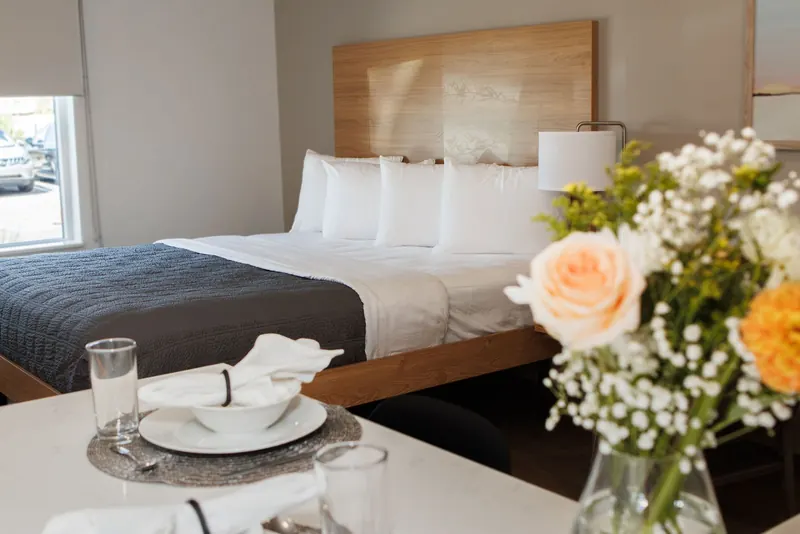 A bright extended-stay suite with a made bed, fresh flowers and a small kitchen