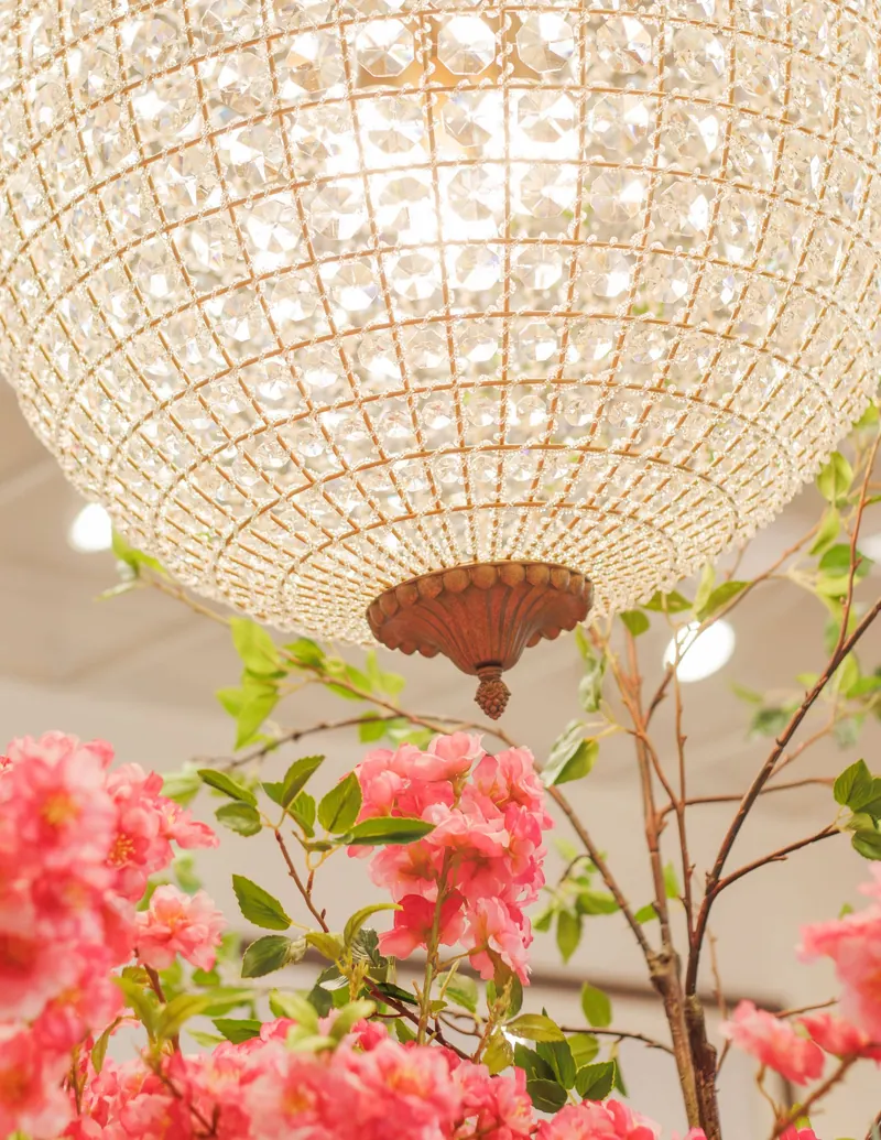 A crystal chandelier glowing above branches of pink blooms inside a home goods shop