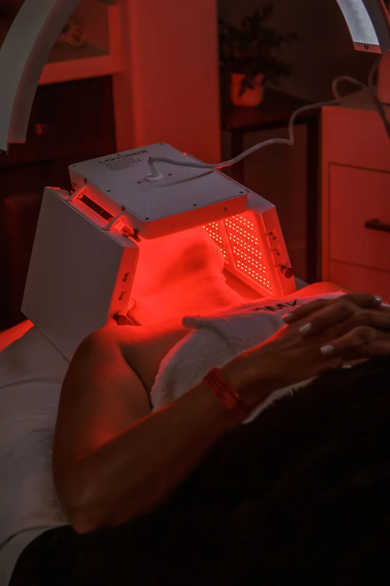 A red LED light therapy panel glowing over a client lying back in a treatment chair