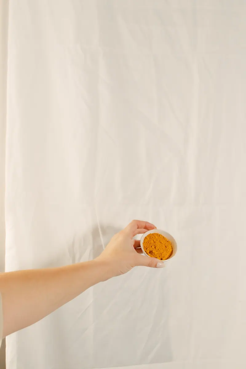 A hand holds up a small glass of golden juice against a cream backdrop
