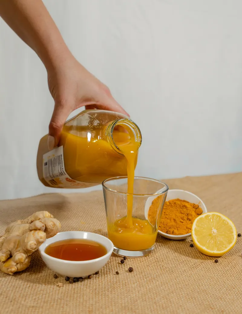 Ginger turmeric juice being poured into small glasses with lemons and fresh ginger