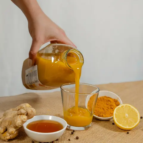 Golden juice being poured into small glasses beside lemons and ginger