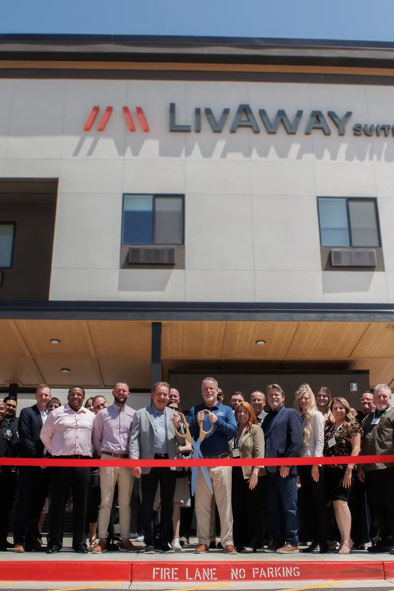 A long line of guests holds a red ribbon under the LivAway Suites sign