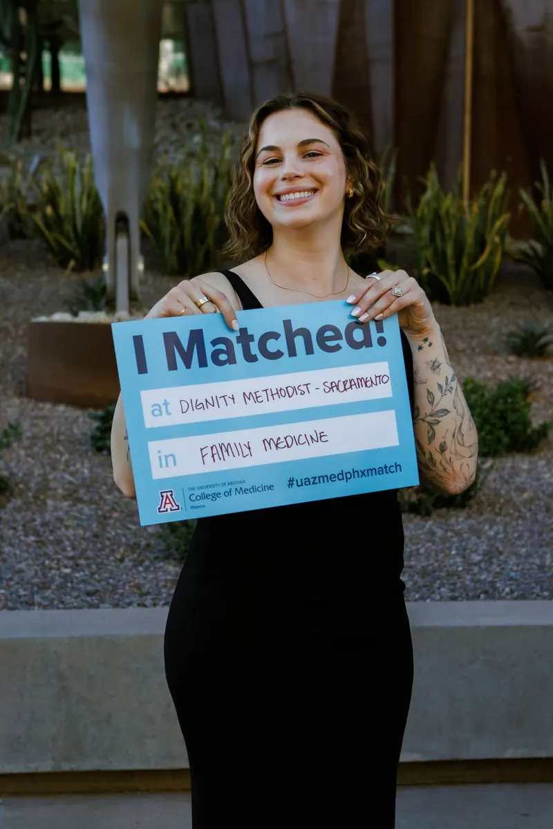 A smiling medical student holds up an I Matched sign at her Match Day celebration