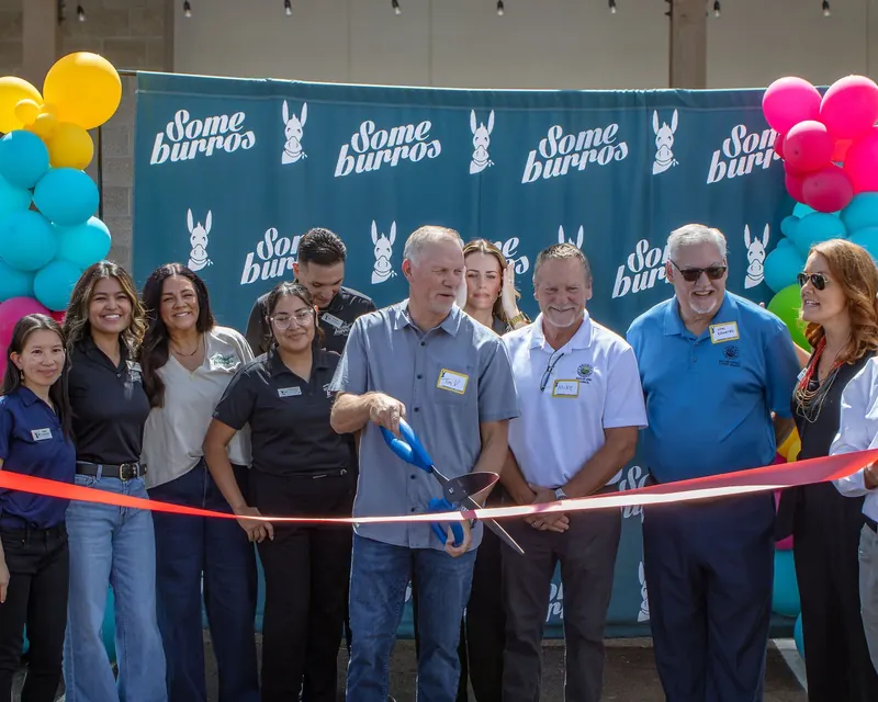 A crowd gathers behind the ribbon under the Someburros banner