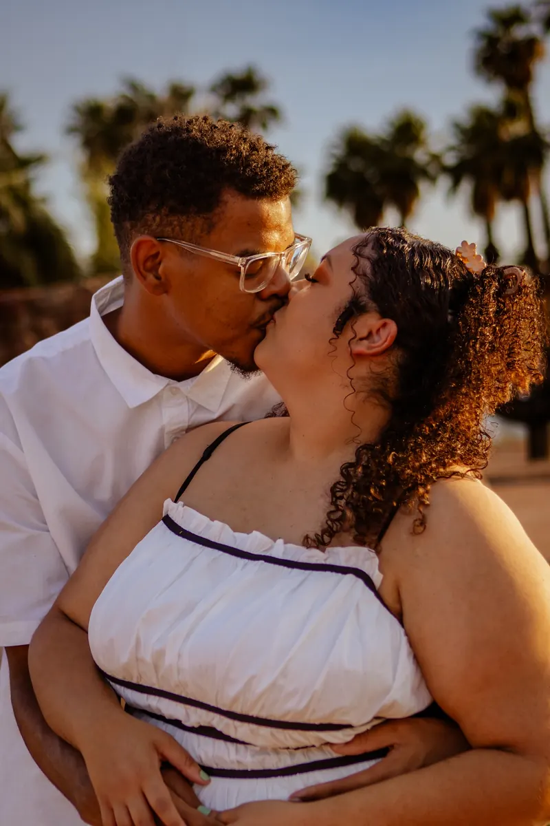 A couple kisses at sunset beneath tall palm trees