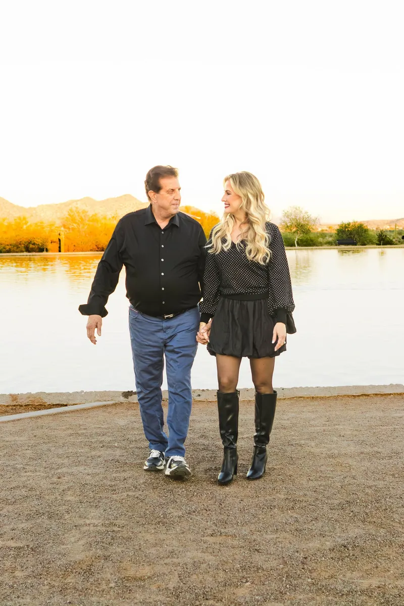 A couple walks hand in hand along a lake at golden hour