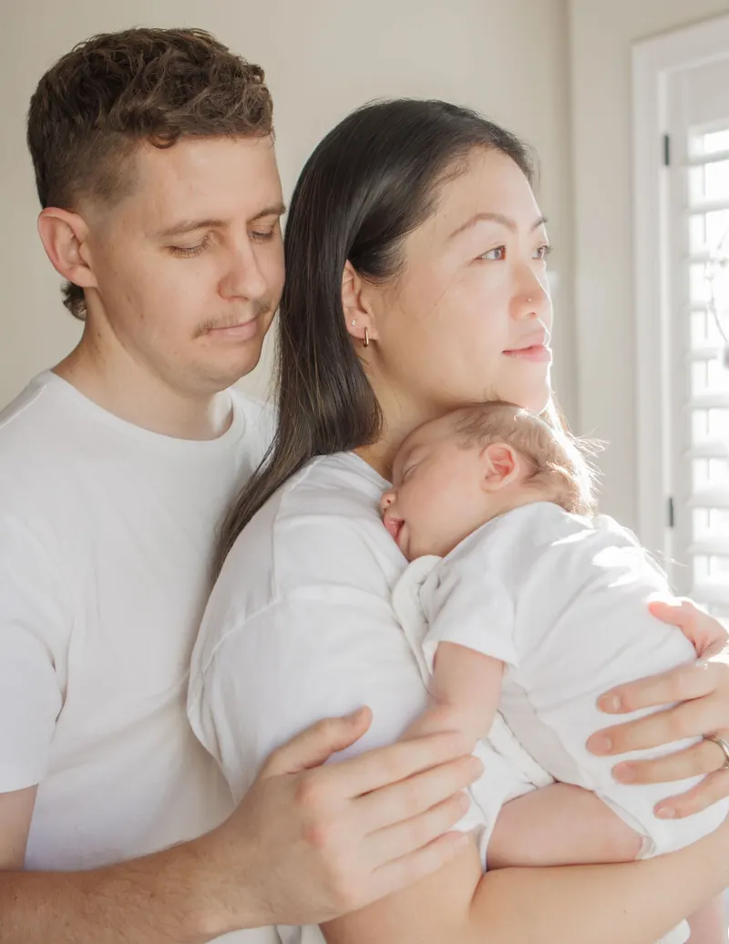 A dad kisses the top of mom's head while she holds their sleeping baby
