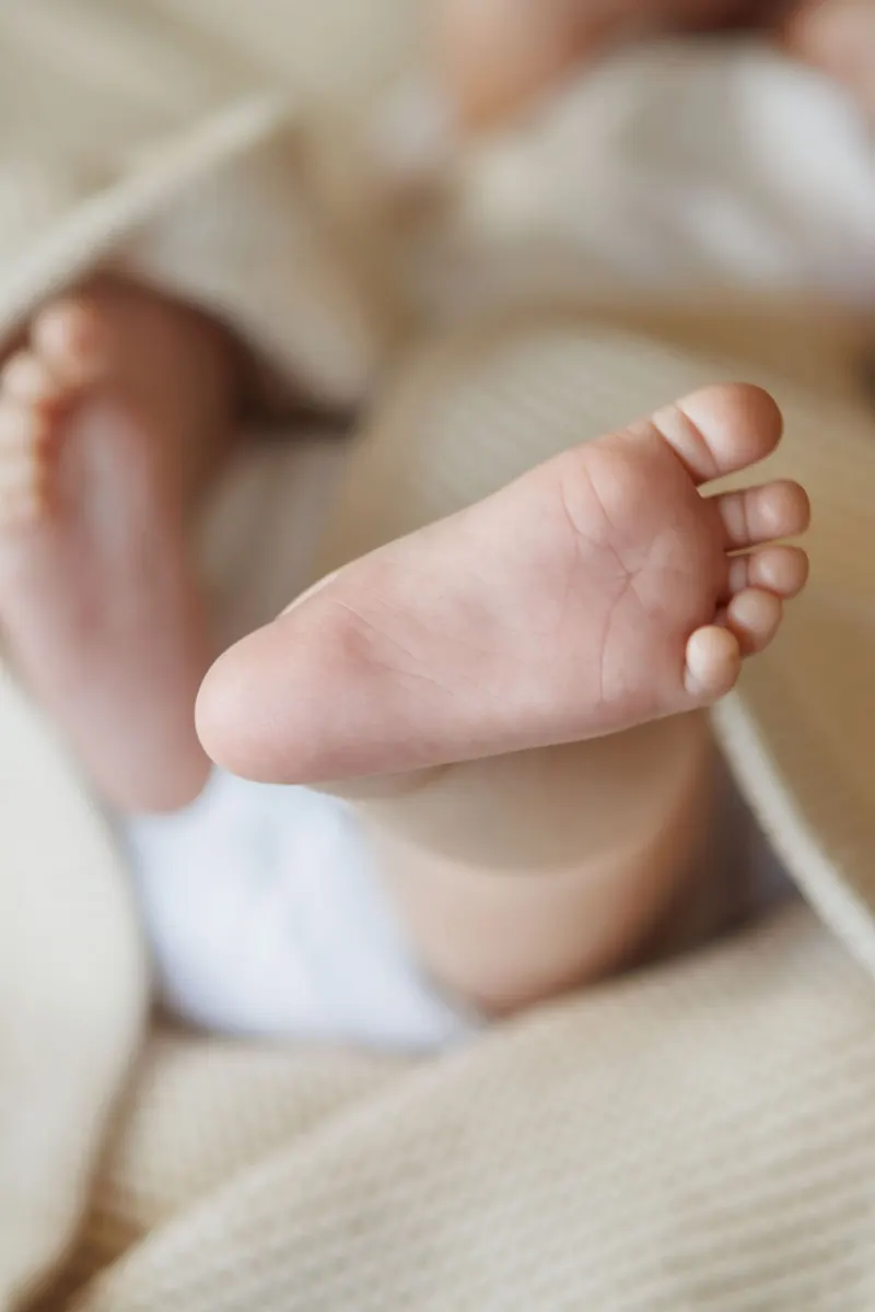 A newborn's feet resting on a cream knit blanket