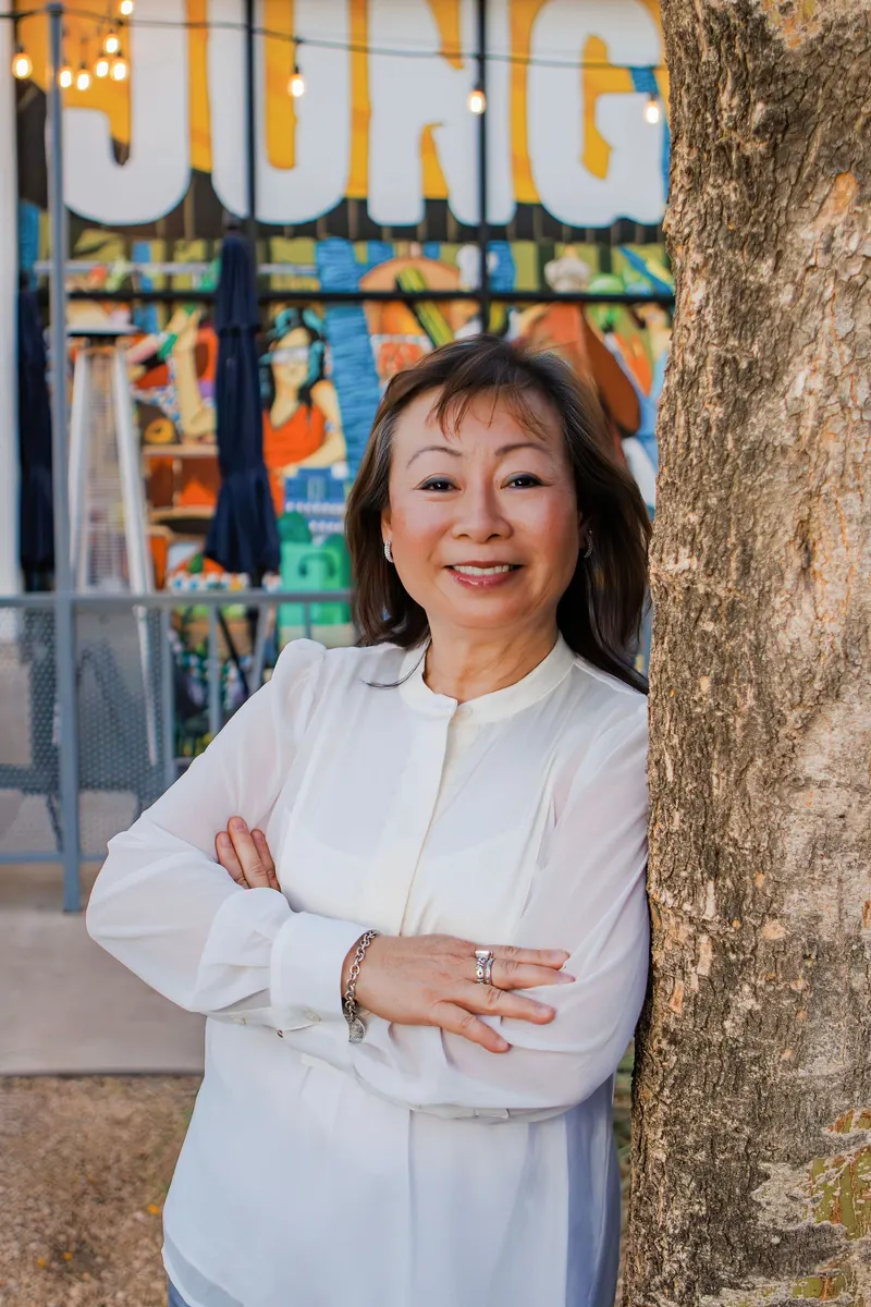 A woman in a white blouse with arms crossed in front of a colorful mural