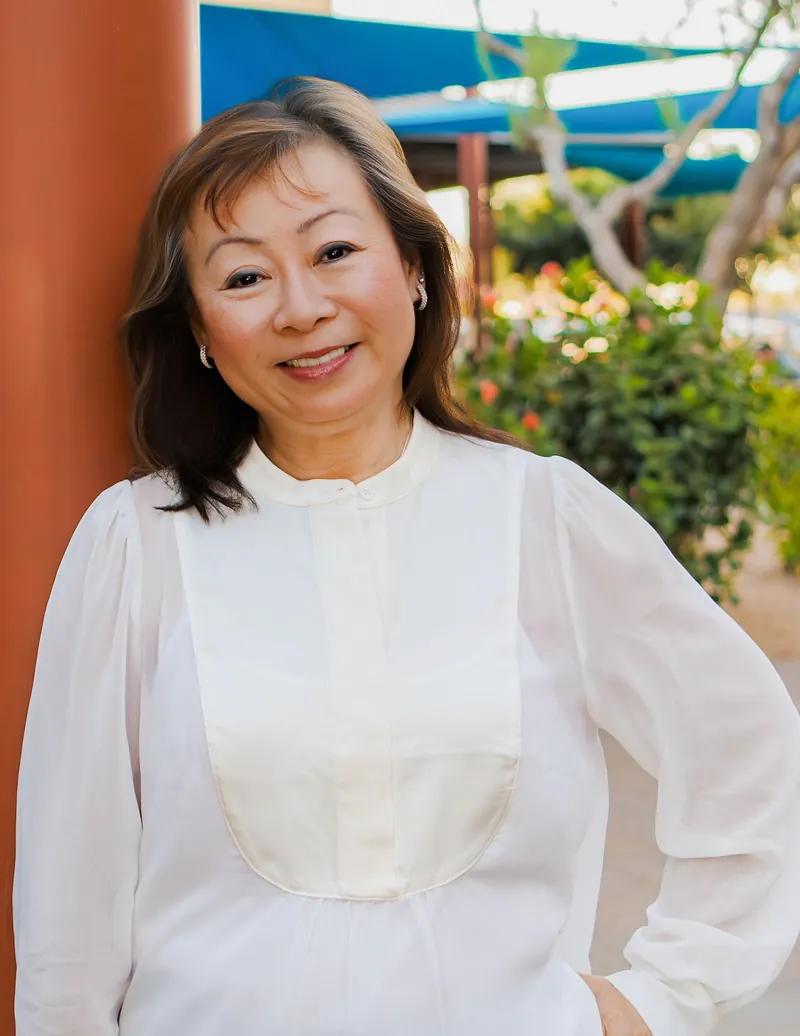 A smiling woman in a white silk blouse leans against a terracotta pillar
