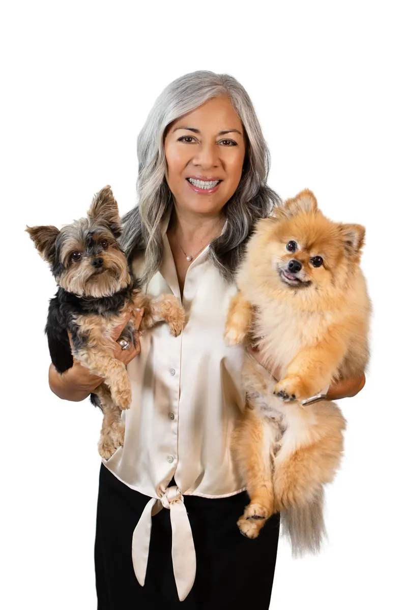 A silver-haired woman holds a yorkie and a pomeranian against a white backdrop